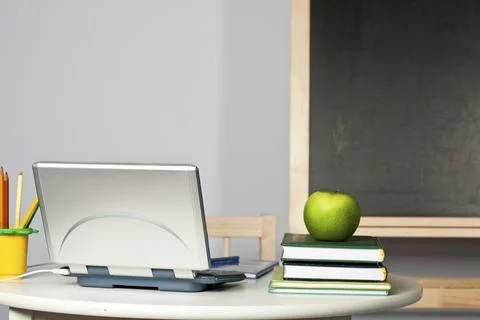 Desk with apple, computer and textbook in class against blackboard. Focus on Stock Photos