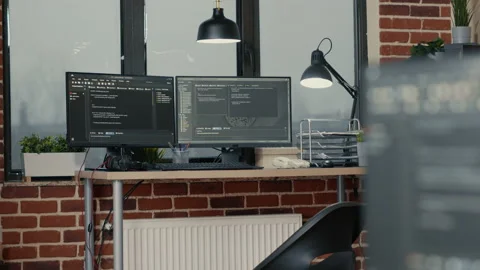 Desk with multiple computer monitors displaying parsing code and programming Stock Footage 168234422