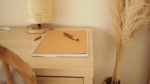 Desk with notebook and pen alongside a decorative plant in a room Stock Footage 345621706