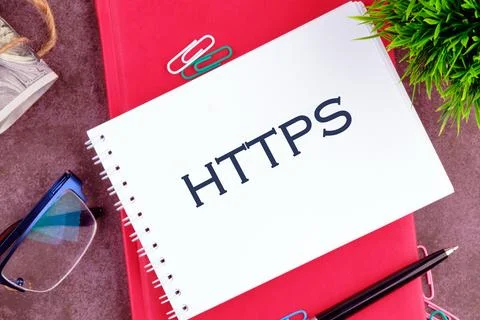 On a desk, a notepad displaying HTTPS is placed along with paper clips, glass Foto stock