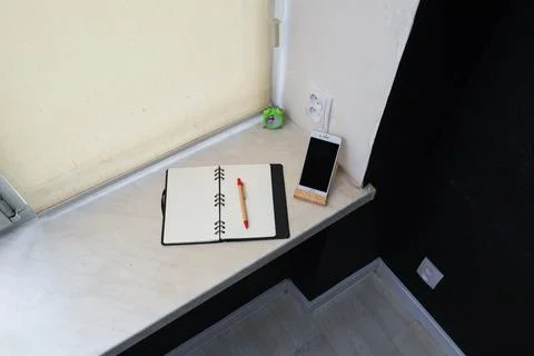 Desk setup with notebook, pen, and smartphone on a windowsill Stock Photos