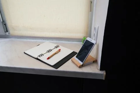 Desk setup with open notebook, pen, and smartphone on a wooden stand Stock Photos