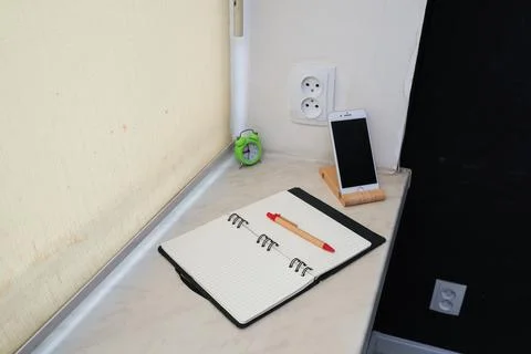 Desk setup with open notebook, pen, smartphone on stand, and alarm clock Stock Photos