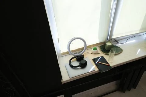 Desk setup with ring light, headphones, and laptop on a windowsill Stock Photos
