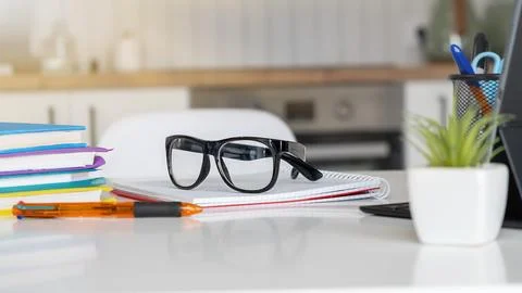 A desk with a stack of books, a pair of glasses, a pen, and a potted plant Foto stock