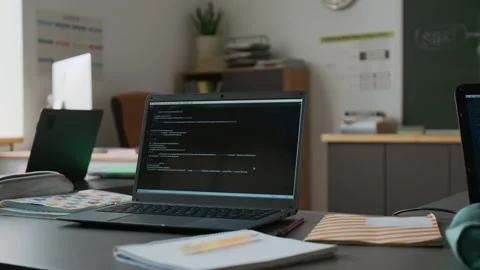 Desk with Two Laptops Displaying Code in Modern IT Classroom with Blackboard Video stock 317634608