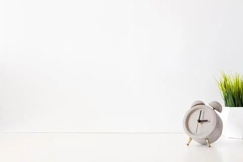 Desk on a white empty wall background with alarm clock and green grass Stock Photos