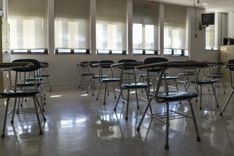 Desks in empty dark high, middle, or elementary school classroom with light Stock Photos