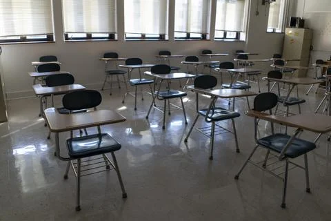 Desks in empty dark high, middle, or elementary school classroom with light Stock Photos