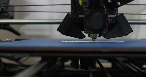 Desktop 3D Printer Nozzle Depositing Filament on Blue Bed, Extreme Close Up Stock Footage 341316337