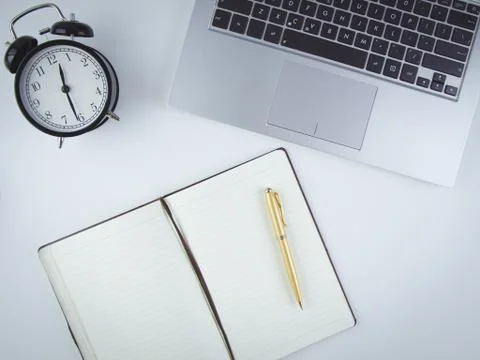 On the desktop is a computer, an alarm clock and a notebook with a pen. Stock Photos