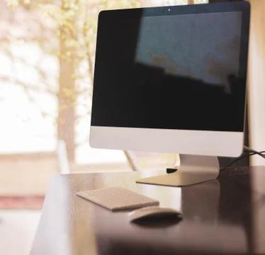 Desktop computer on wooden table against light window with trees Stock Photos