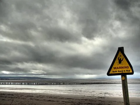 Desolate beach with warning sign for soft sand and mud Stock Photos