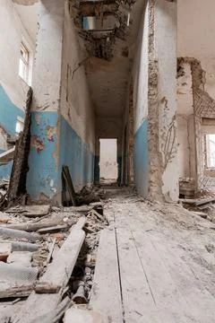 Desolate hallway of ruined structure with peeling blue paint, collapsed ceili Stock Photos