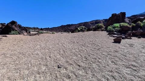 A desolate landscape characterized by rocky terrain and a vast, bright blue sky Stock Photos