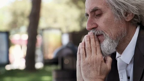 Desperate gray-haired man in a suit cries and prays in the Park Stock Footage 96543112