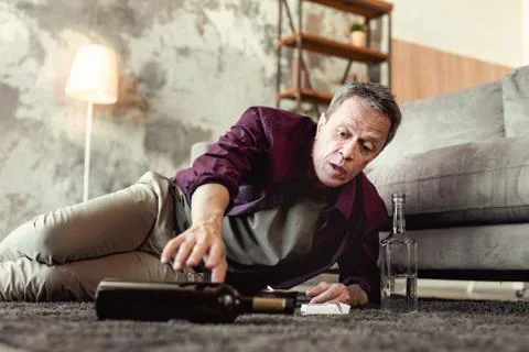 Desperate grey-haired guy reaching out for bottle of wine 库存照片