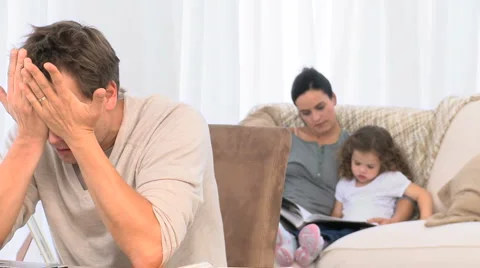 A desperate man on his laptop while his family is on the sofa Stock Footage 1017484