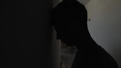 Desperate man hitting head against wall with dark copy space Stockbeeldmateriaal 346244047