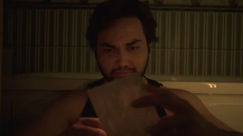 A desperate man reads a letter while sitting on the floor and holding a candle. Stock Footage 127710971