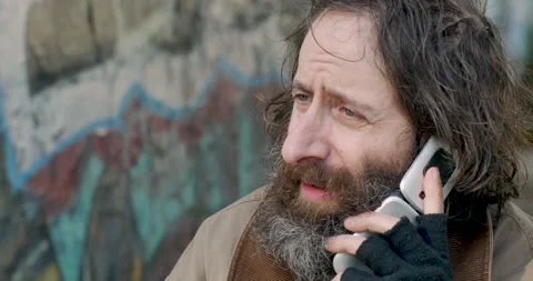 Desperate man talking on a flip phone while people walk by outside on the street Stock Footage 143516181