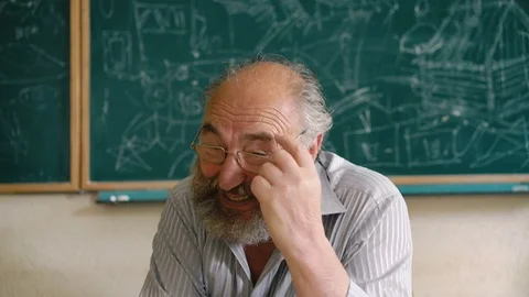 Desperate old male teacher sitting at the desk and rubbing head 4K Stock Footage