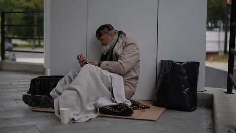 Desperate retired homeless man using smartphone sitting on cold winter street Stock Footage 292182199