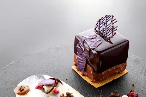 Dessert with nuts in chocolate glaze in the shape of a cube on black slate Stock Photos