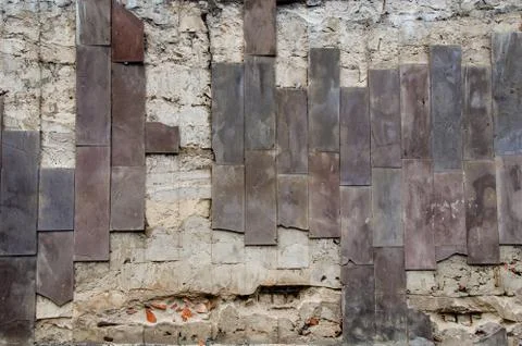 A destroyed wall with narrow vertical brown tiles. Stockfoto's