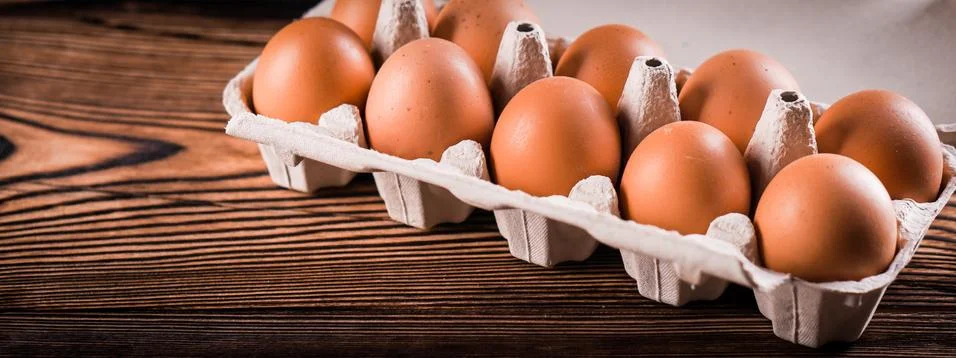 Detail close-up of chicken eggs in egg box on the old brown wooden background. Stock Photos