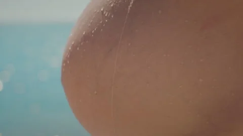A detail of a drop of water sliding down a pregnant woman belly in soft sunlight Stock Footage 285744346