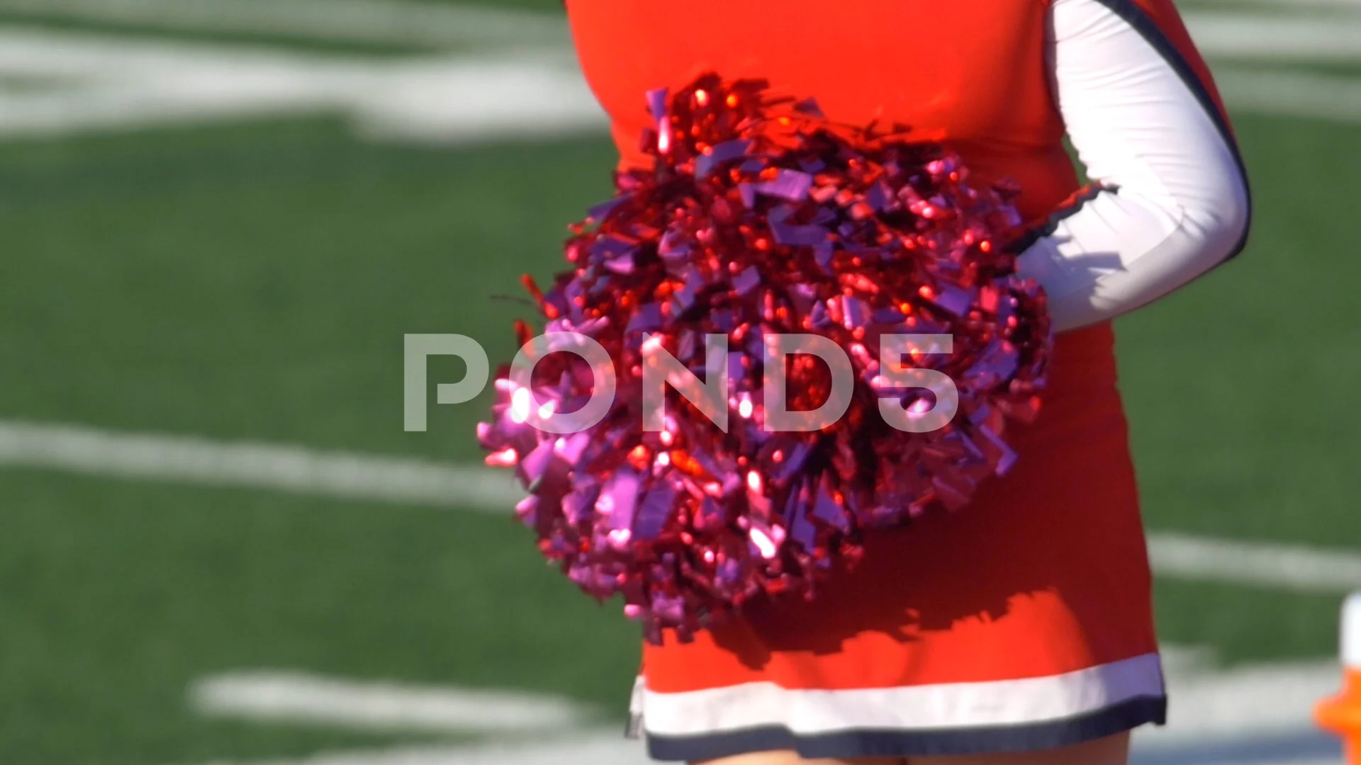 Cheerleaders doing routine with pom poms on football field, Stock