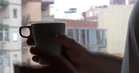 Detail of a man with a cup of tea observing from the window Stock Footage 129555964