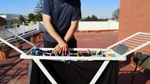 Detail of man picking up clothes from the clothesline on the terrace at home Stock Footage 236860244