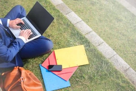 Detail of a man typing on the laptop, while sitting on the grass Stock Photos