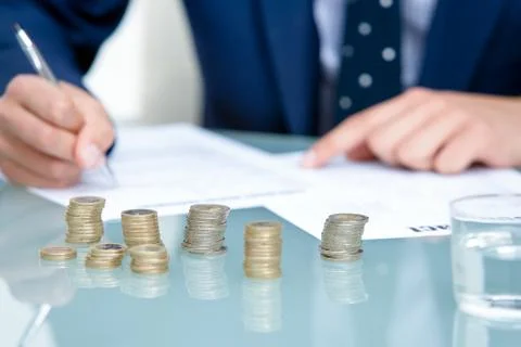 Detail of money coins with hands writing in background. Stock Photos