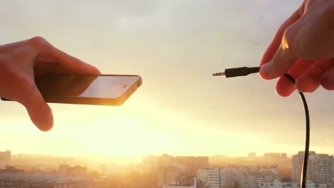 Detail of stereo jack being plugged into smartphone with sunset on background Stock Footage 83707967