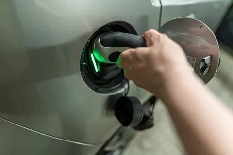 Detail view at a mans hand with is plugin the electric charging wire and plug Stock Photos