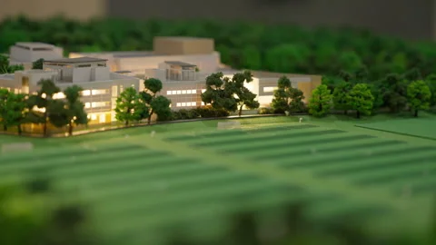 A detailed 3D architectural model is lit up, surrounded by miniature trees and Видео 336031420