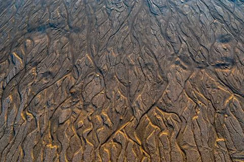 A detailed close-up captures wavy patterns in sand beneath shallow water Stock Photos