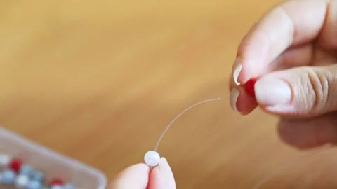 Detailed close up of hands threading red and white beads for intricate bead.. Stock Footage 339566455
