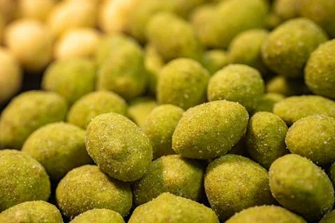 A detailed close-up of two varieties of peanuts, one with a green spice. Stock Photos