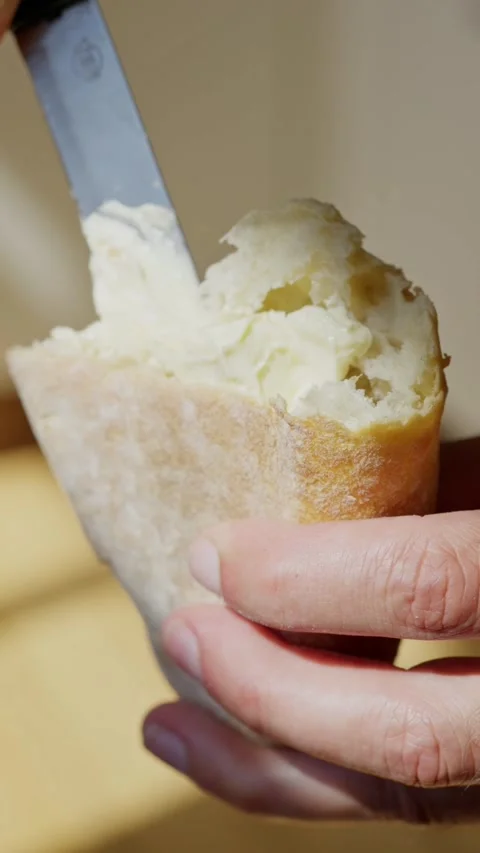 A detailed closeup of a hand gently spreading luscious butter on a fresh piece Stock Footage 313601396