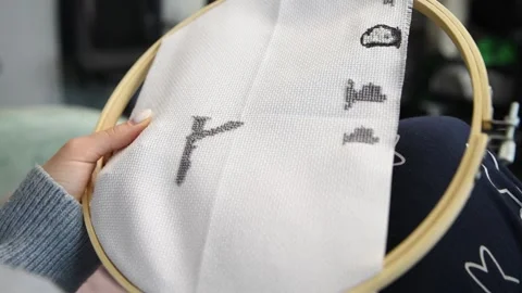 Detailed hands stitching gray cross stitch pattern on white fabric in woode.. Stock Footage 334955110