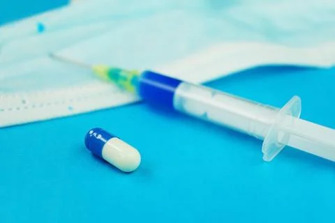 A detailed macro of a syringe by pills with needle on a medical mask with b.. Stock Photos
