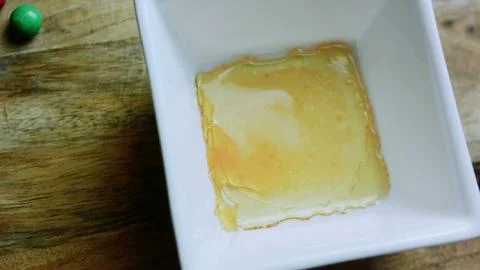 Detailed serving study of pouring amber caramel into a white square mold Stock Photos