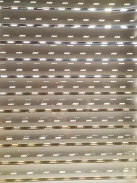 This detailed texture of a closed security shutter showcases light peeking th Stock Photos