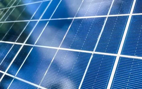 Detailed view of a blue solar panel surface reflecting sky and green trees .. Stock Photos