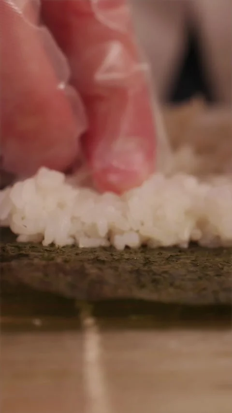 Detailed view of wet hands pressing sticky rice onto seaweed sheet Stock Footage 337119152
