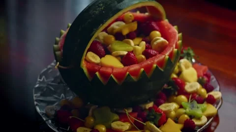 Detailed watermelon handle arching over mixed fruit in warm light, 4K Vidéo 341115106